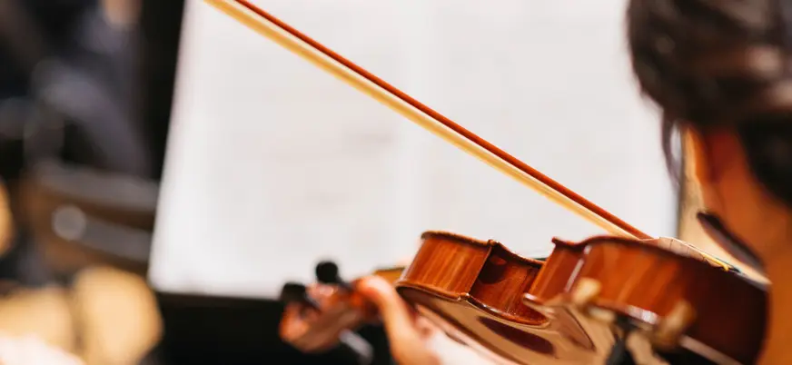 Manos tocando un violín durante un concierto en Viena, en primer plano, con la partitura desenfocada al fondo.