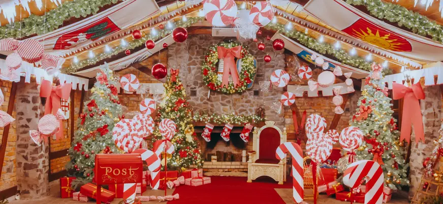 Decoración navideña en una sala con chimenea, árboles iluminados, guirnaldas, bastones de caramelo y adornos rojos, creando un ambiente festivo típico de la Navidad.