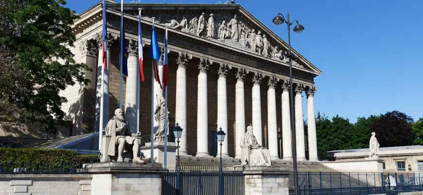 Palacio Borbón en París con columnas y banderas francesas.