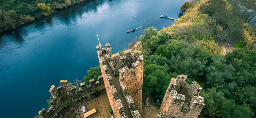 Vista aérea del castillo de Almourol junto al río y un barco navegando cerca.