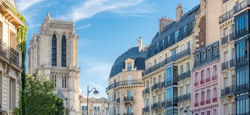 Edificios históricos en París con fachada de piedra y tejados inclinados bajo cielo parcialmente nublado.