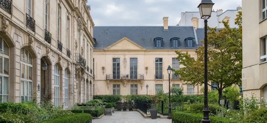 ardín francés frente al Hôtel de Sully en el barrio del Marais, París, con setos geométricos y fachada renacentista.