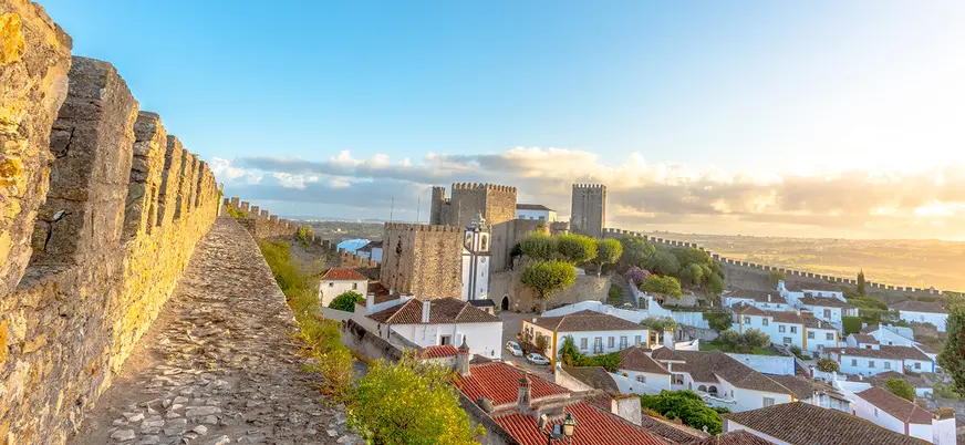 Murallas y castillo de Óbidos al atardecer con vistas al pueblo de casas blancas.