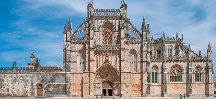 Fachada del Monasterio de Batalha con detalles góticos y visitantes en la plaza.