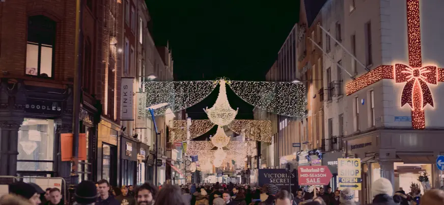 Calle de Dublín decorada con luces navideñas y adornos en la noche, con numerosos peatones paseando y tiendas iluminadas a ambos lados.
