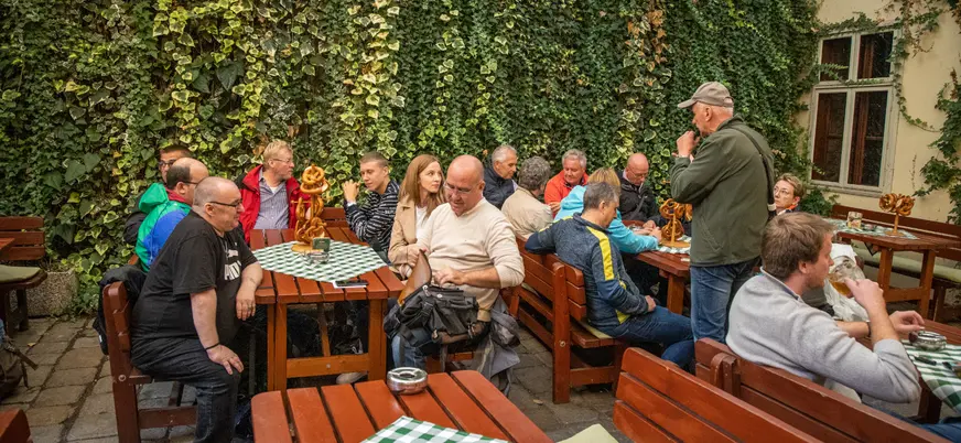 Grupo de participantes del tour de comida y bebida por Bratislava escuchan las explicaciones del guía en una cervecería local.