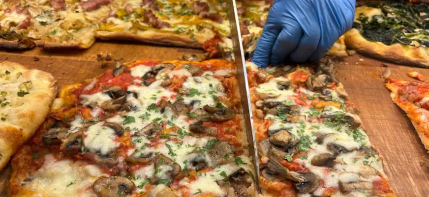 Pizzero italiano cortando una pizza con purchetta, otra de las recetas típicas que se prueban en este tour gastronómico por el barrio de Trastevere.