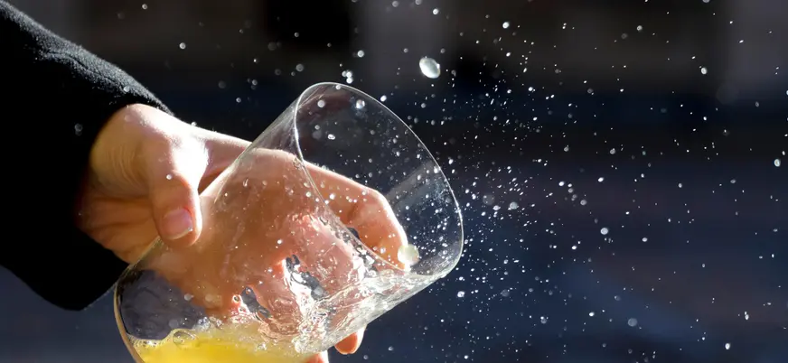 Mano sosteniendo un vaso de sidra asturiana mientras se escancia, con gotas salpicando, símbolo de la tradición sidrera.