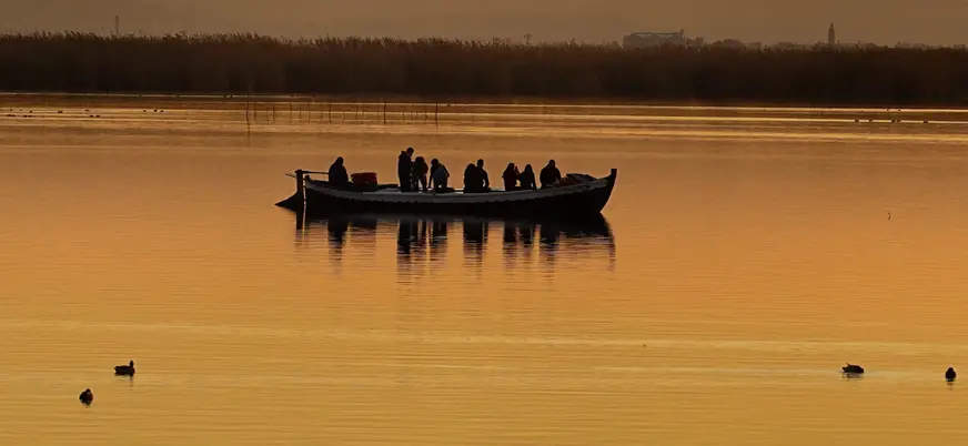 Una barca tradicional cruza el lago mientras el sol se refleja en el agua. 