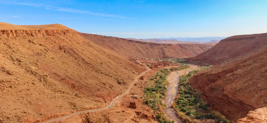 Vista panorámica de las carreteras serpenteantes del Alto Atlas entre colinas áridas y un río rodeado de vegetación