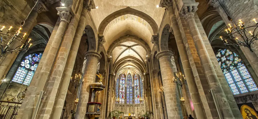 Interior gótico de la Basílica de San Nazario en Carcasona, con vitrales, columnas y bancos de madera.