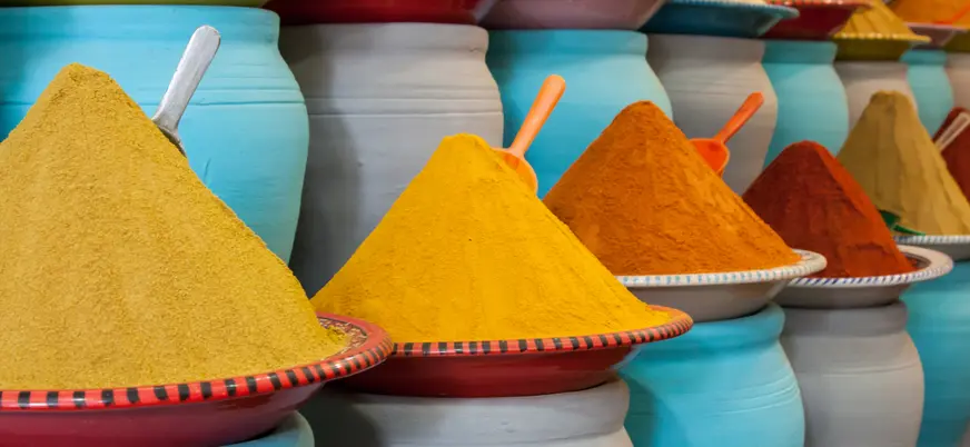 Montículos de especias tradicionales marroquíes en tonos cálidos, dispuestos en mercados locales sobre recipientes de cerámica.