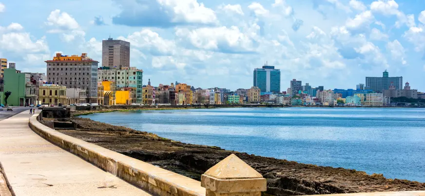 Vista del Malecón habanero con el mar al atardecer y el skyline de edificios coloniales al fondo.