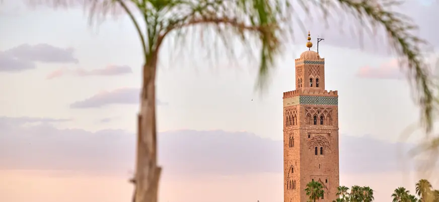 Minarete de la mezquita Koutoubia de Marrakech enmarcado por palmeras al atardecer, símbolo de la ciudad.