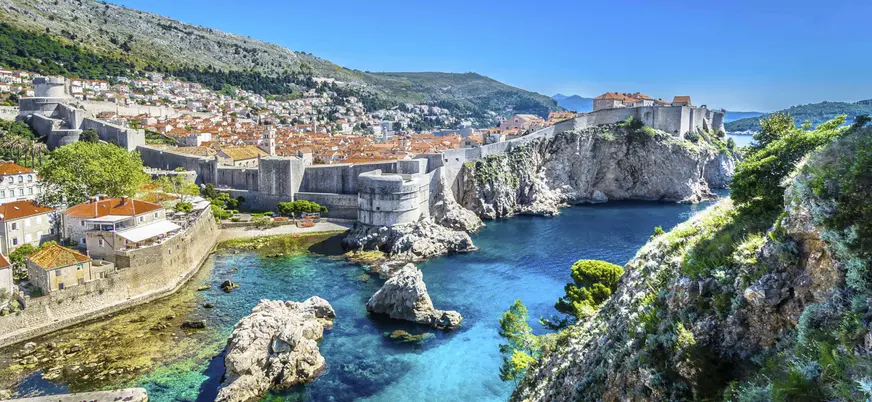 Murallas de Dubrovnik bordeando la costa, acantilados y aguas turquesas desde un punto elevado.