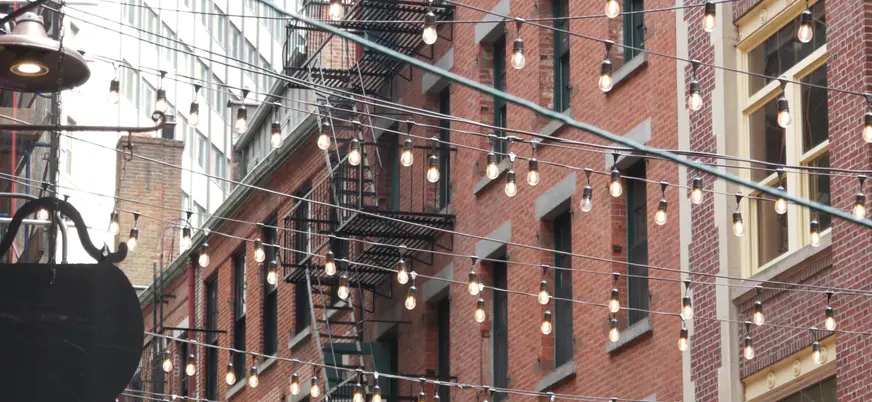 Calle Stone Street en Nueva York con luces colgantes y fachadas de ladrillo estilo histórico.
