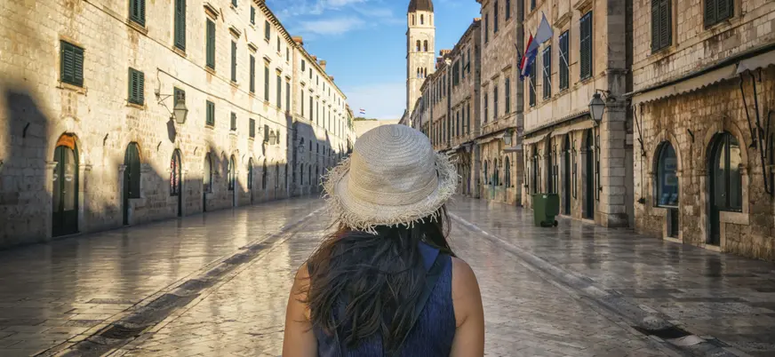Mujer con sombrero paseando por la calle Stradun de Dubrovnik, al fondo la torre del reloj del casco antiguo.