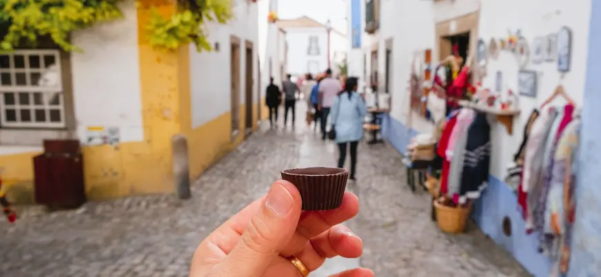 Mano sosteniendo una ginjinha en vaso de chocolate en una calle de Óbidos