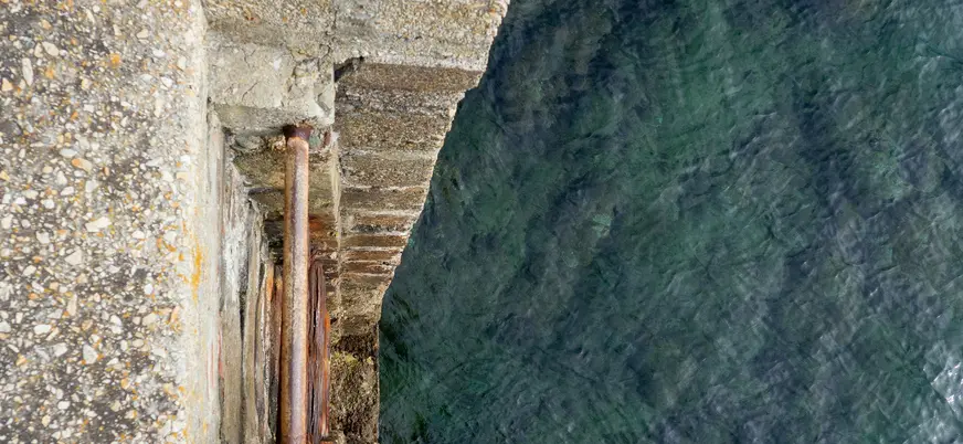 Escalera de piedra con barandilla oxidada que desciende hacia el agua clara del puerto de Cudillero, en la costa asturiana.