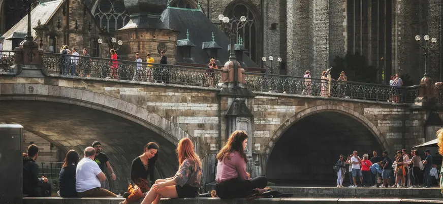 Personas paseando y descansando junto a un puente en el centro histórico de Gante