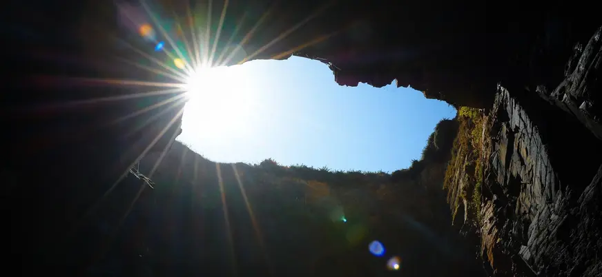 Interior de cueva en la Playa de las Catedrales, Ribadeo, Galicia, con el sol brillando intensamente.