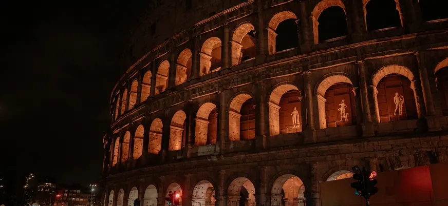 Coliseo de Roma iluminado de noche y esculturas visibles desde la calle