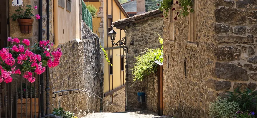 Callejón empedrado con casas de piedra y flores rosas en Potes, Cantabria