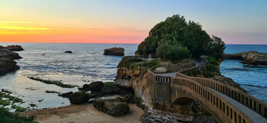 Atardecer en Biarritz, Francia, con el puente de piedra que conecta la costa con la Rocher de la Vierge, mar azul.