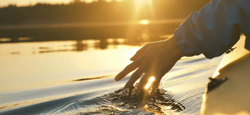 Mano rozando el agua desde un kayak al atardecer en Es Grau, Menorca