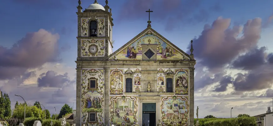 Fachada colorida de la Iglesia de Santa Maria de Válega en Portugal, cubierta con azulejos y campanario lateral.