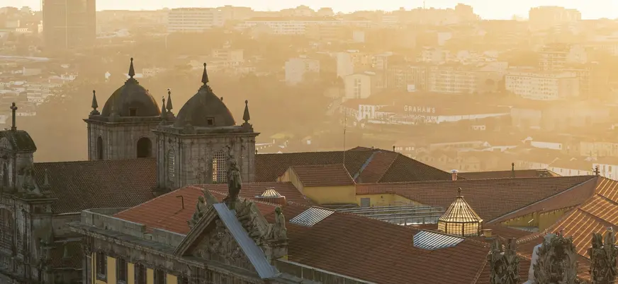 Vista de Oporto al atardecer con tejados históricos y la ciudad iluminada por luz dorada.