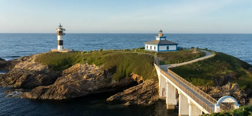 Faro de la Isla Pancha en Lugo, conectado por un puente a la costa. Edificio y torre blanca y negra junto al mar.