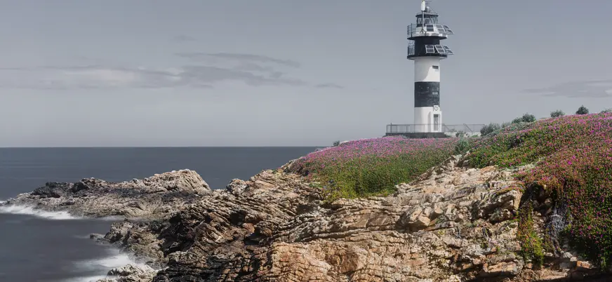 Faro de Isla Pancha en Ribadeo, sobre un acantilado cubierto de flores silvestres y con el mar Cantábrico al fondo.