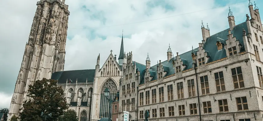 Torre de San Rumoldo y edificios históricos de la Grote Markt en Malinas (Mechelen), Bélgica, bajo cielo nublado.