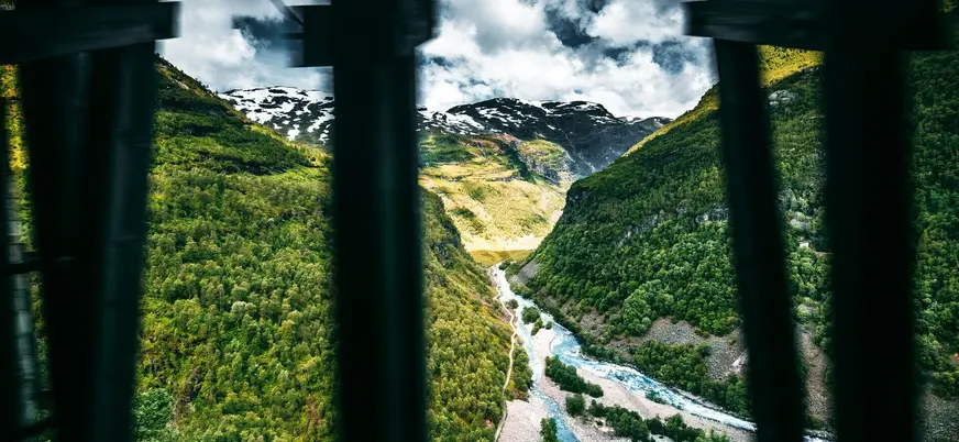 Vista impresionante del valle y río Kjosfossen desde Myrdal, Noruega, con frondosos bosques y montañas nevadas.