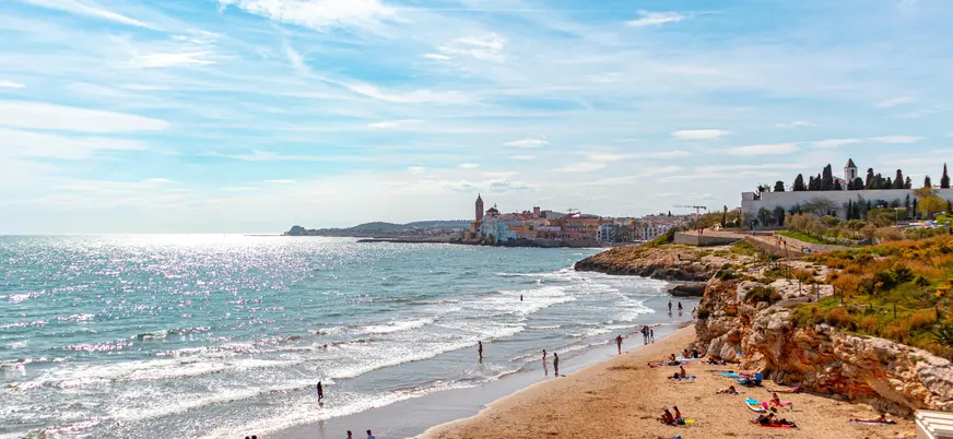 Vista costera de Sitges con casas junto al mar y acantilados bañados por las olas.