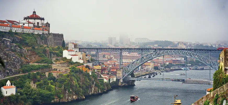 Vista del puente de Don Luis I con barcos navegando por el Duero en día de niebla.