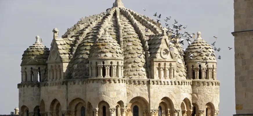 Cúpula bizantina de escamas pétreas de la Catedral de Zamora, España, con un grupo de palomas volando.