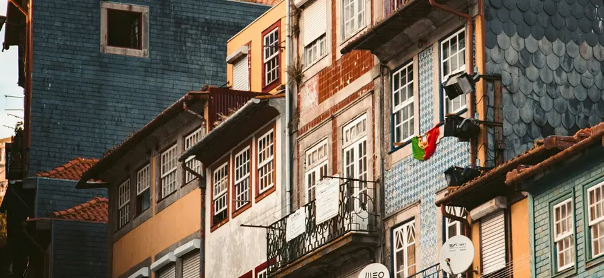 Fachadas coloridas y tradicionales de Oporto con balcones, azulejos y una bandera portuguesa.