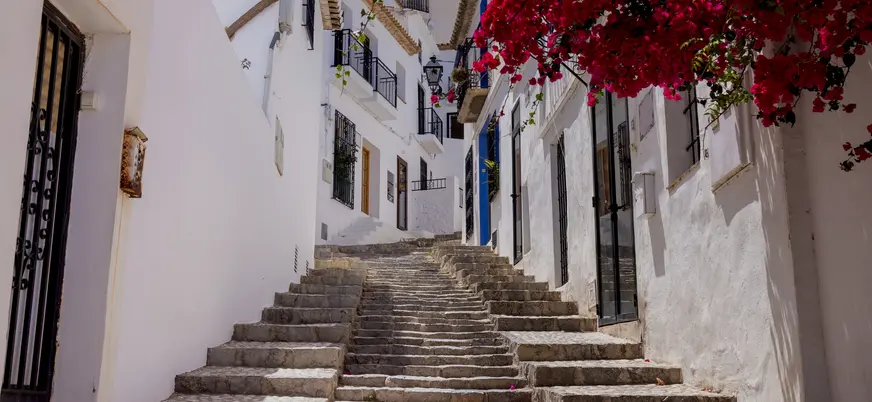 Calle empedrada de casas blancas en Altea, con buganvillas rosas colgando.