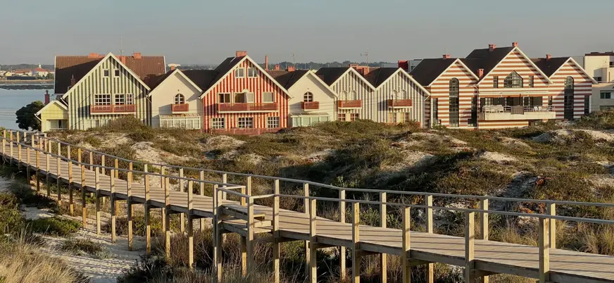 Casas a rayas de Costa Nova junto a pasarela de madera entre dunas.