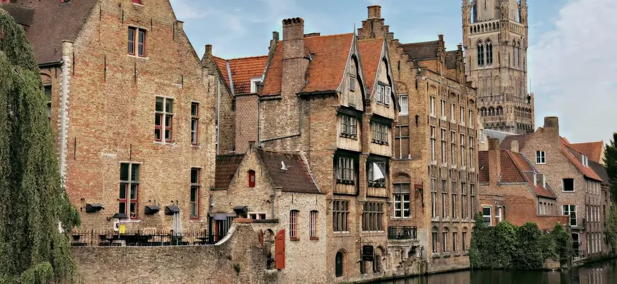 Casas medievales de ladrillo junto a un canal de Brujas, Bélgica, con el campanario.
