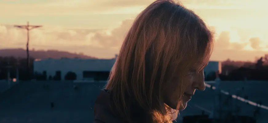 Mujer con cabello rojizo al atardecer en el Santuario de Fátima, silueta de la cruz y la Basílica de la Santísima Trinidad.