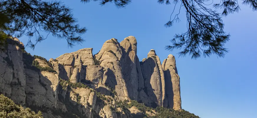 Formaciones rocosas puntiagudas y verticales de la montaña de Montserrat, Barcelona, con cielo azul en un día soleado.