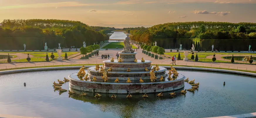 Fuentes en el exterior del Palacio de Versalles, rodeadas de jardines bien cuidados y arquitectura clásica.