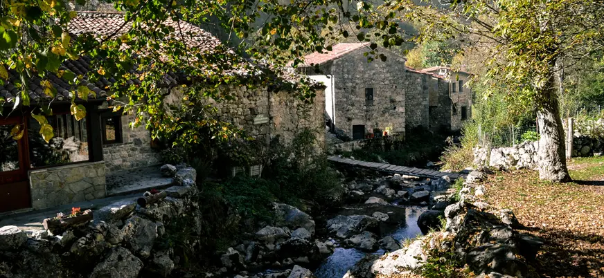 Pueblo de Bulnes, Asturias, con casas de piedra, un arroyo y un pequeño puente de madera en Picos de Europa.