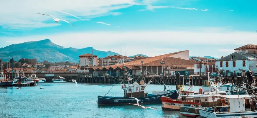 Barcos pesqueros en el puerto de San Juan de Luz con montañas al fondo.