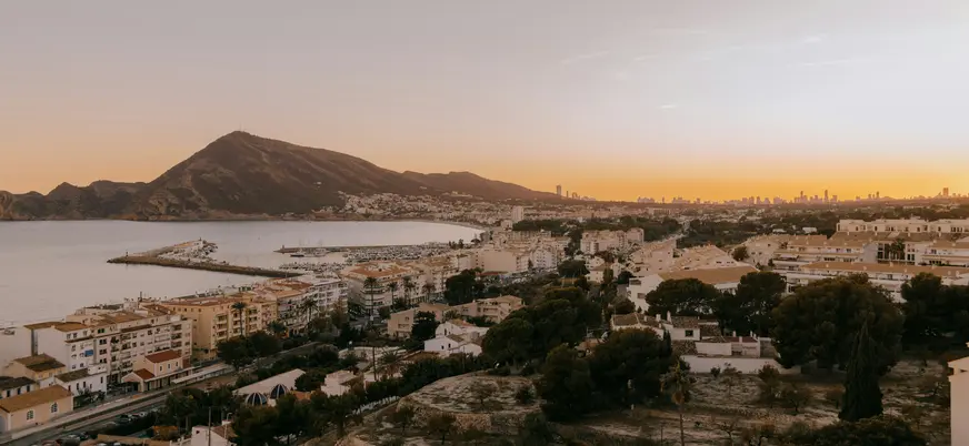 Vista aérea de Altea al atardecer, mostrando la costa, el puerto, las casas blancas y la montaña de fondo.