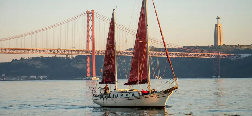 Velero navegando frente al Puente 25 de Abril y el Cristo Rei en Lisboa