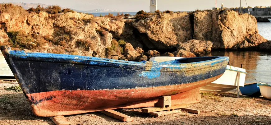 Barca de pesca tradicional azul y roja varada en la orilla de Tabarca con acantilados y el mar de fondo.